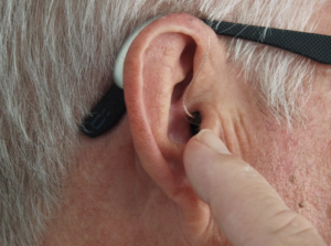 An older person pointing to their hearing aid