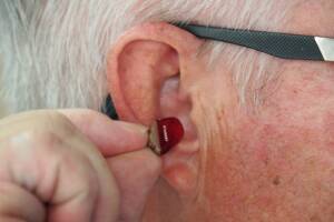 A person putting a red hearing aid in their ear